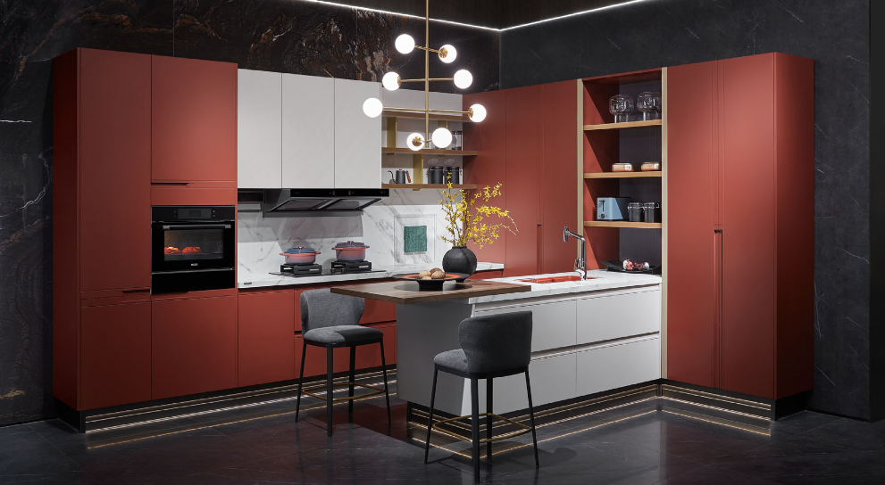 Cocina en L con frentes rojo óxido, isla marfil y zoclo con iluminación indirecta