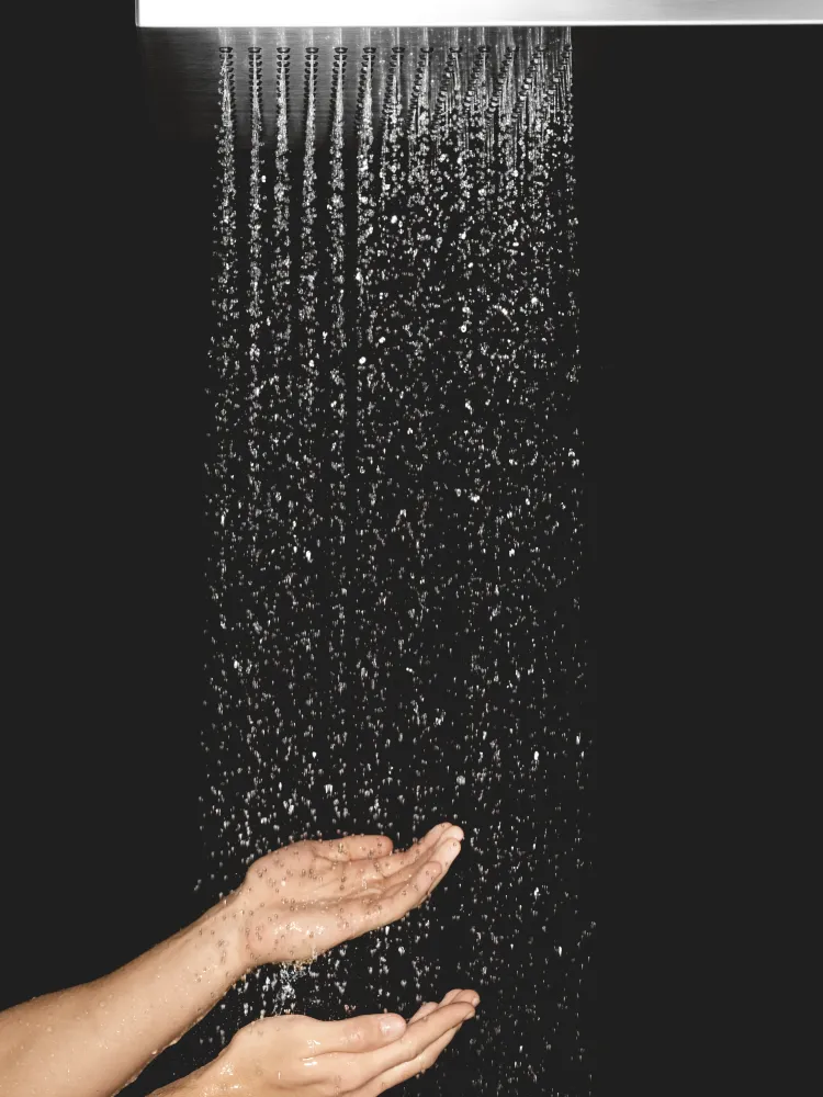 Detalle de una descarga de regadera tipo lluvia sobre fondo negro con manos recibiendo el agua